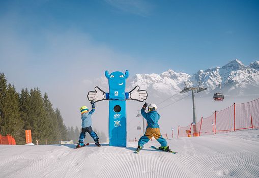 Kinder fahren auf einer Funslope an einem blauen Maskottchen vorbei.