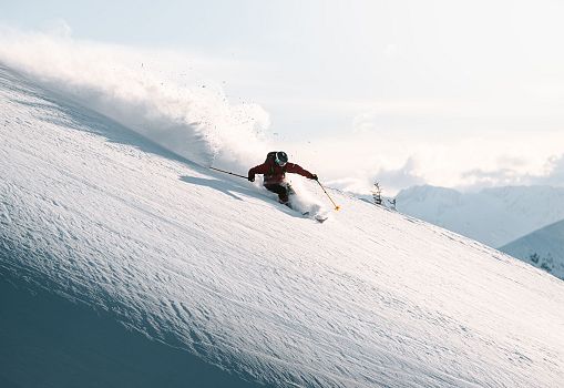 Freerider skiing powerfully through deep powder snow on a steep slope.
