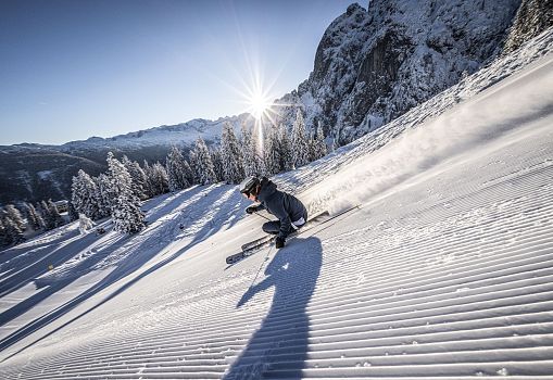 Ein Skifahrer carvt bei Sonnenaufgang auf einer frisch präparierten Piste.