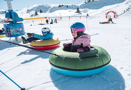 A child riding a snow tube in the children's area of a ski resort.