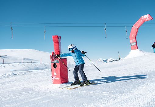 Ein Kind fährt auf einer verschneiten Funslope an einem interaktiven Spielelement vorbei.