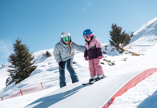 Ein Erwachsener begleitet ein Kind beim Skifahren auf einer verschneiten Funslope.