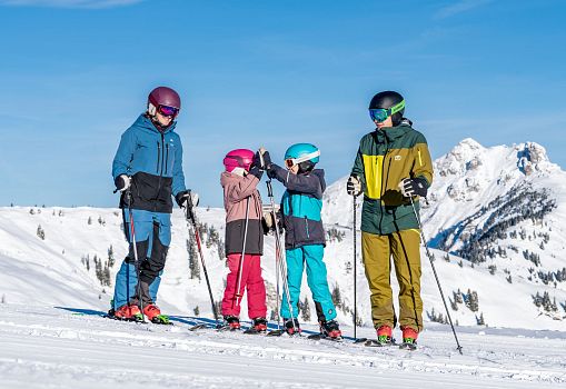 Eine Familie steht mit Skiern auf einer sonnigen Piste in den Bergen.