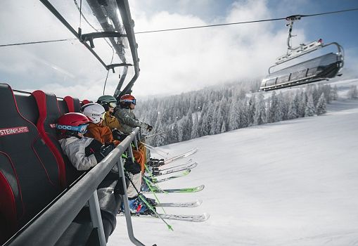 A family sitting on a chairlift above a snowy landscape.