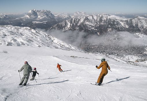A family skiing down a snowy slope with mountain views.