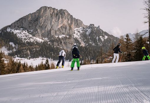 Several skiers skiing on a freshly groomed slope with an impressive mountain backdrop.