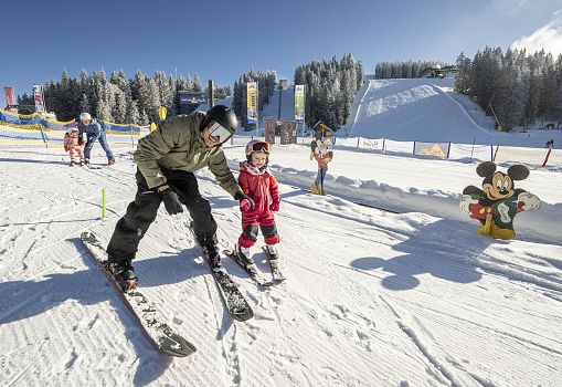 An adult teaching a child to ski in a kids’ ski area.
