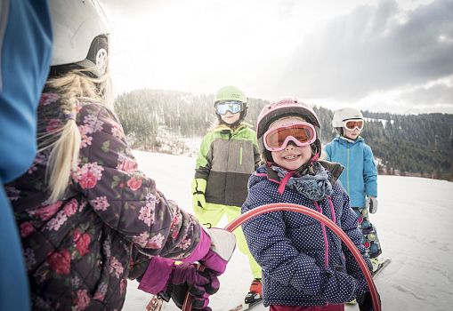 Kinder in Skikleidung üben gemeinsam das Skifahren auf einer verschneiten Piste.