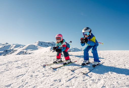 Two children happily skiing on a sunny slope in the high mountains.
