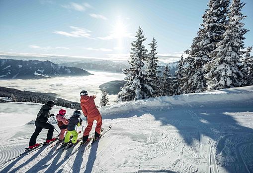 A family with children enjoys the winter view at Schmittenhöhe under the sunshine.