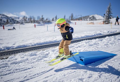 A child skiing over a box in a fun park.