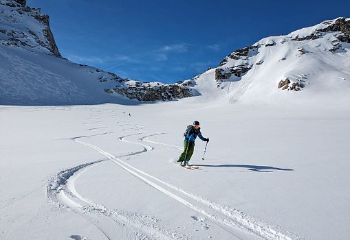A ski tourer making tracks through untouched powder snow in the mountains.
