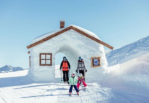 Skiing family with children passing through a snow house in the Alpbachtal funslope.