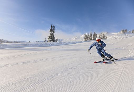 Ein Skifahrer carvt auf einer breiten, frisch präparierten Piste bei Sonnenschein.