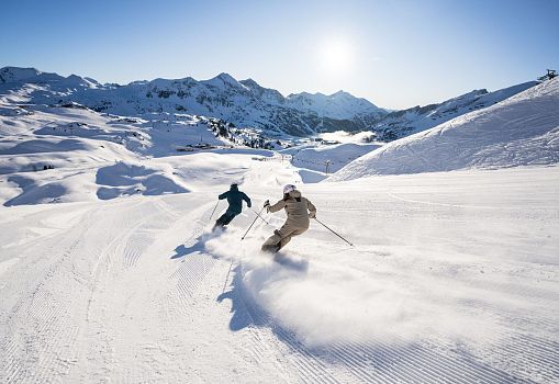 Zwei Skifahrer fahren bei Sonnenaufgang die Piste in Obertauern hinunter.