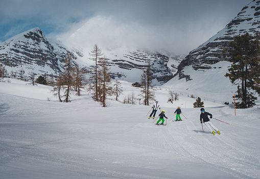 A family skiing in the Wurzeralm on a snowy slope surrounded by mountains.