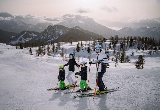 A family standing with skis on the Wurzeralm, looking at the surrounding mountains.