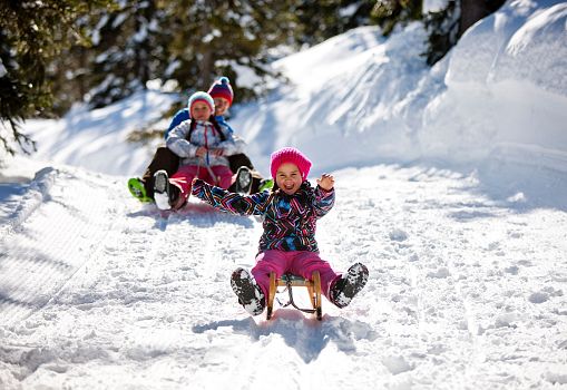 Children happily tobogganing down a snowy hill on the Planneralm.