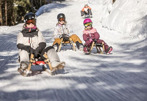 Eine Familie rodelt gemeinsam auf einer verschneiten Rodelbahn.