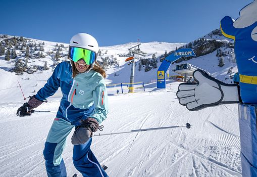 A skier smiling while skiing on a sunny funslope in a ski resort.