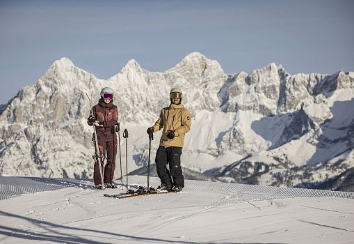 Two skiers standing on a sunny slope with impressive mountain views.