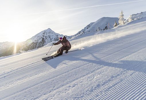 A skier carving on a freshly groomed slope at sunrise.