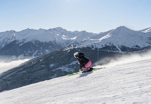 A skier carving down a snowy slope with mountains in the background