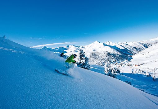 A skier skiing through fresh powder with an impressive mountain landscape.