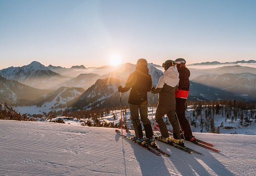 A group of skiers enjoying the sunrise on a snowy slope with mountain views
