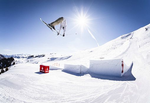 Ein Skifahrer springt über einen Kicker und greift die Skispitzen.