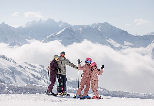 A family standing with skis on a snowy slope with an impressive mountain panorama.