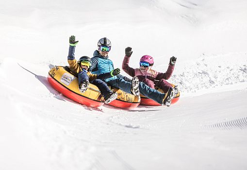A man and two children ride down the snow tubing track on tyres.