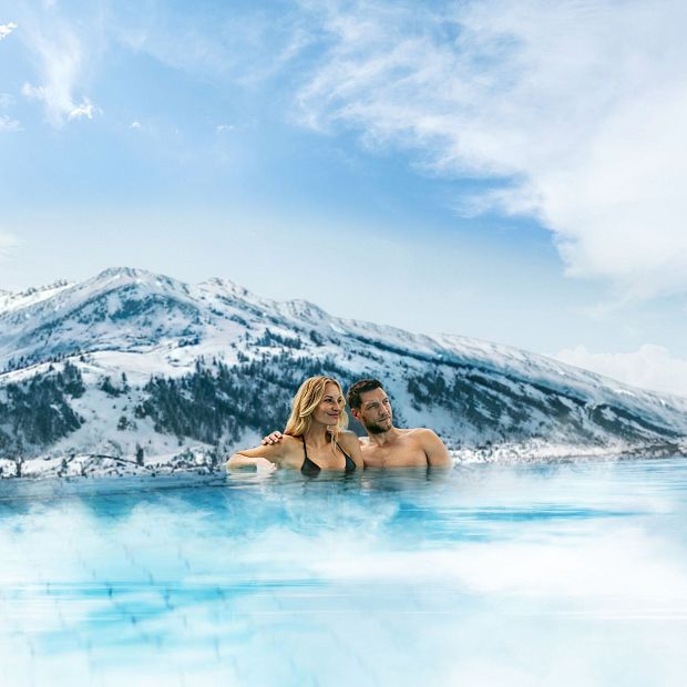 A couple relaxing in a warm outdoor pool with snowy mountain views