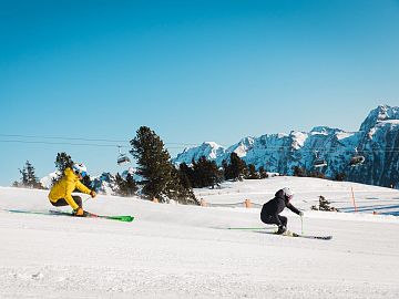 Zwei Skifahrer fahren eine sonnige Piste am Fanningberg hinab.