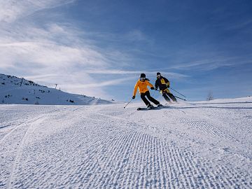 Zwei Skifahrer fahren hintereinander auf einer frisch präparierten Piste.