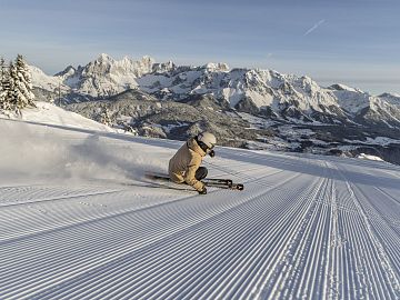A skier carving on a freshly groomed slope with mountain views.