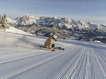 Ein Skifahrer carvt auf einer frisch präparierten Piste mit Bergpanorama.