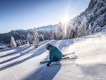 Ein Skifahrer carvt durch Pulverschnee bei Sonnenschein in Dachstein West.