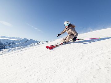 A skier carving on a sunny slope with a snowy mountain panorama.