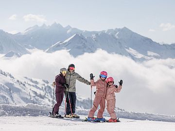 A family standing with skis on a snowy slope with an impressive mountain panorama.